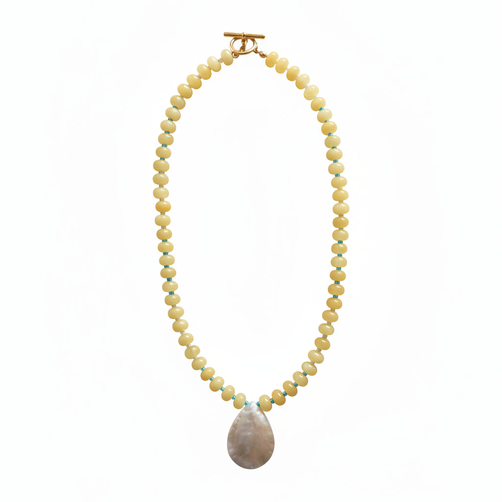 A beaded necklace with small pale yellow beads accented by thin blue and green stripes, featuring a large iridescent shell pendant and a gold toggle clasp, displayed on a plain light background.