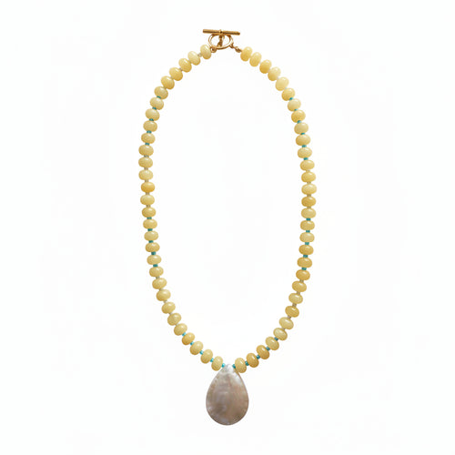 A beaded necklace with small pale yellow beads accented by thin blue and green stripes, featuring a large iridescent shell pendant and a gold toggle clasp, displayed on a plain light background.