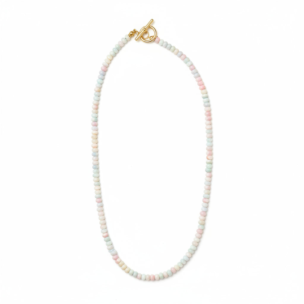 A delicate beaded necklace with small pastel-colored beads in white, pink, and light blue, featuring a gold clasp, laid flat on a light beige background.