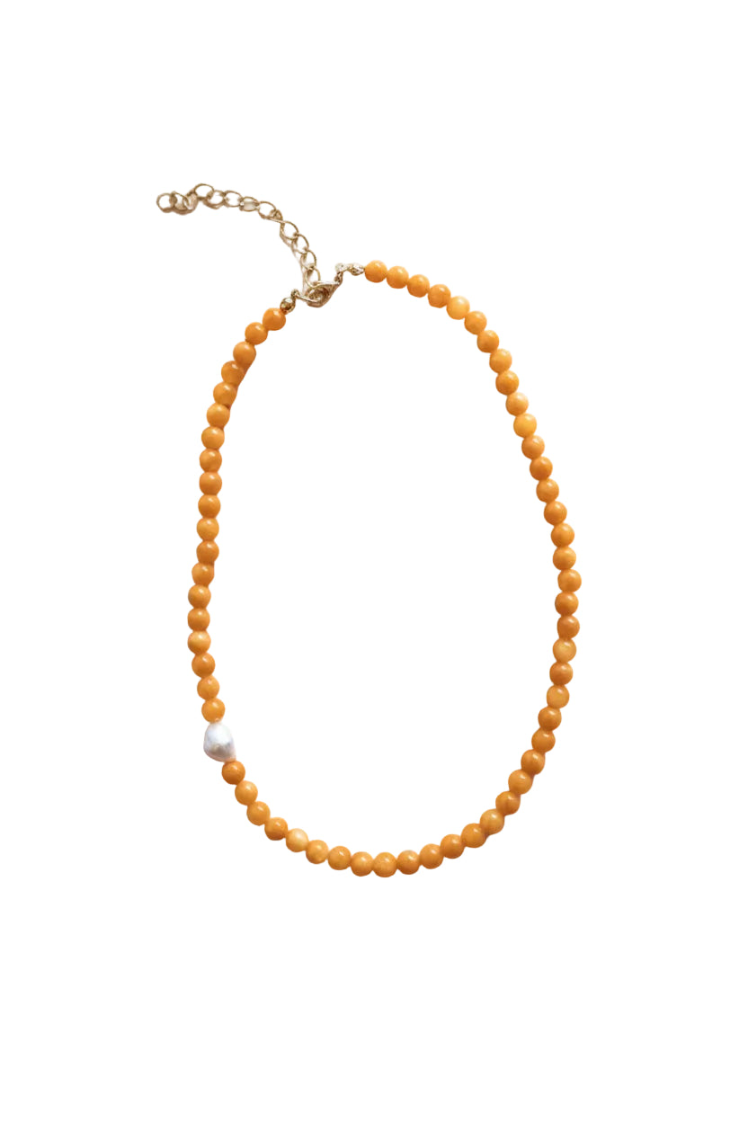 A beaded necklace made of small round orange beads with a single white pearl accent and a gold-tone chain extender, shown on a plain light background.
