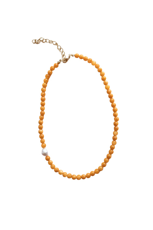 A beaded necklace made of small round orange beads with a single white pearl accent and a gold-tone chain extender, shown on a plain light background.